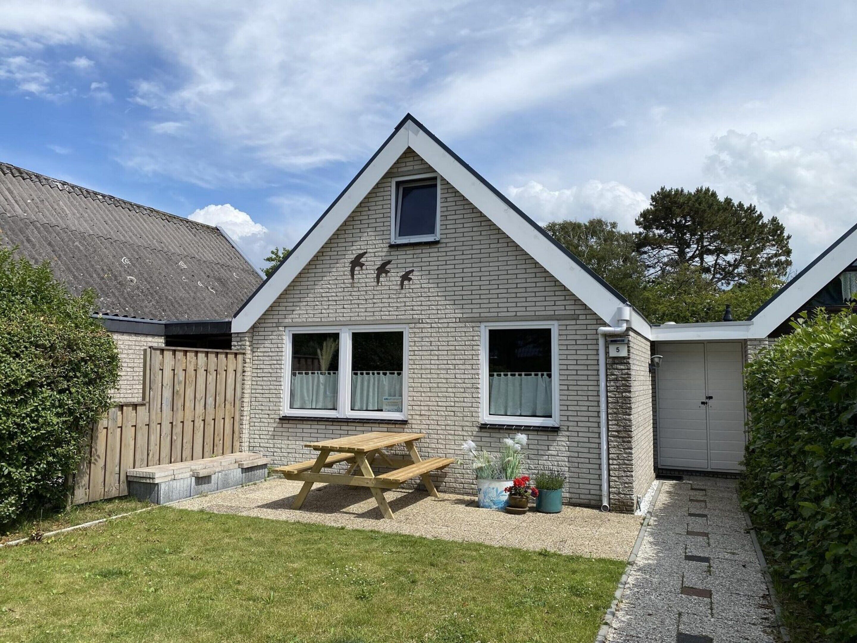 A two-story house with a sloped roof, a wooden fence, a picnic table, and a garage.