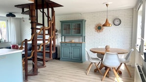 A kitchen with a wooden spiral staircase, teal cabinets, a round dining table with white chairs, and a hanging pendant light. - Relaxing Holiday Home Near Beach (Sint Maartensvlotbrug)