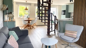A modern living room with a grey sofa, a striped armchair, and a small white table. A wooden spiral staircase connects the living room to the kitchen area. - Relaxing Holiday Home Near Beach (Sint Maartensvlotbrug)