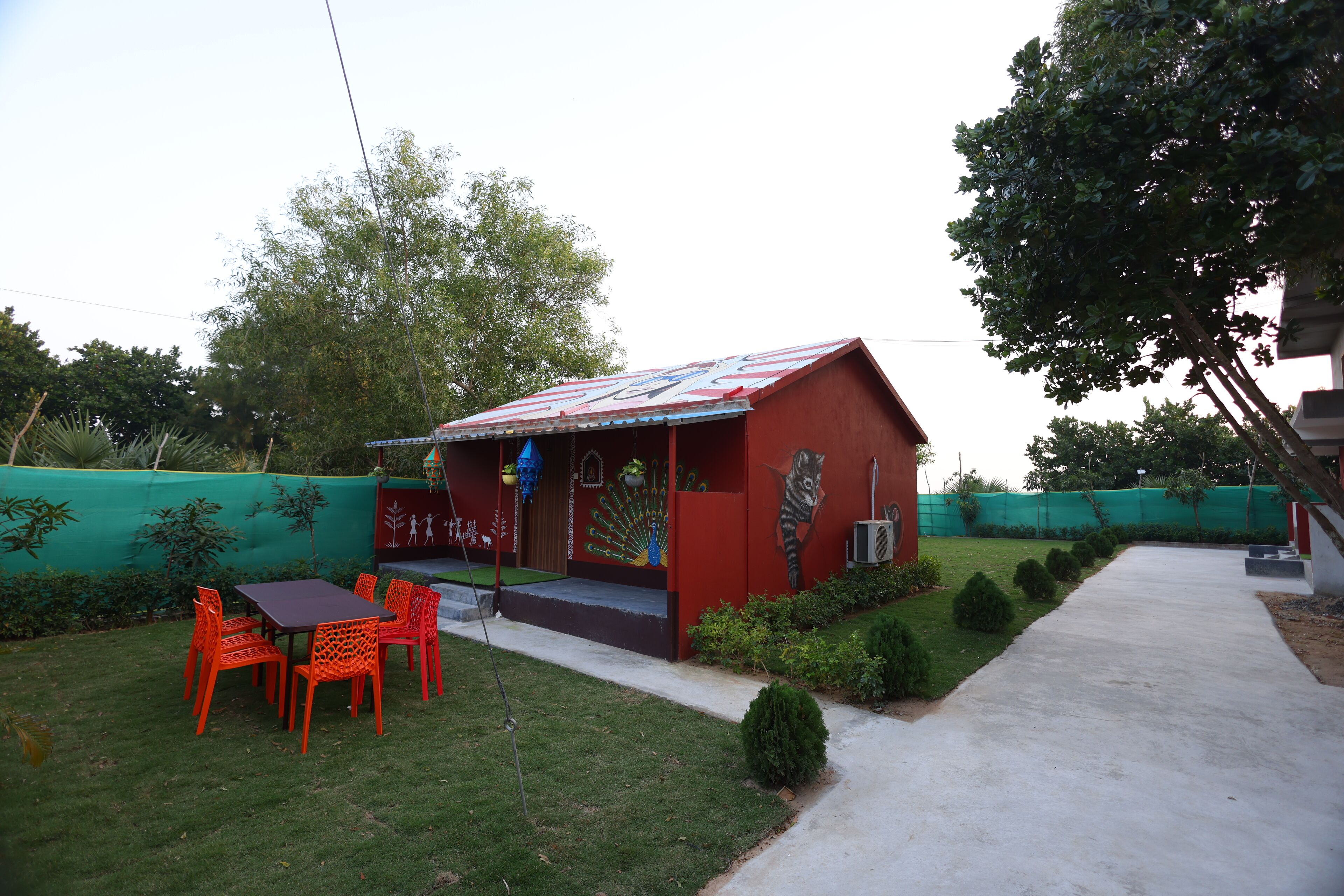 A small red building with a colorful roof, surrounded by a green fence and a paved path.