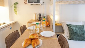A breakfast setup with croissants, juice, and a coffee maker on a wooden table in a room with a bunk bed and a small TV. - Stylish & fully equipped apt. only 5 min to metro. Nice area near the Bastille.  (Paris)