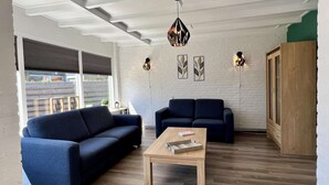 A modern living room with two dark sofas, a wooden coffee table, and a white brick wall with leaf-patterned artwork. - Appealing Holiday Home for Family (Sint Maartensvlotbrug)