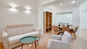 A modern living room with a sofa, a glass coffee table, and a dining area with chairs and a table.