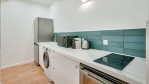 A compact kitchen with a washing machine, a built-in oven, and a coffee maker.