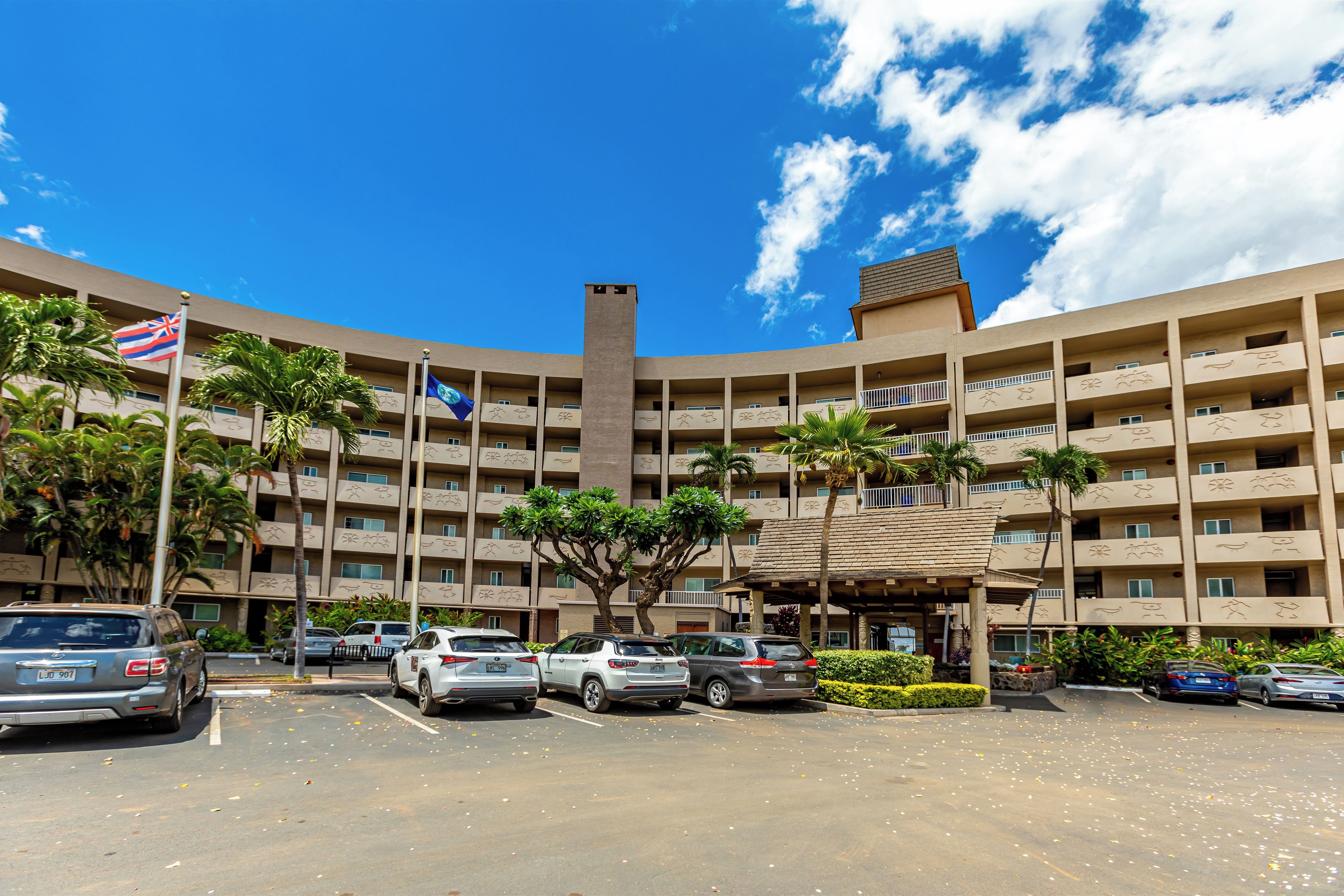 Un hotel de varios pisos con un patio central, palmeras y una bandera.