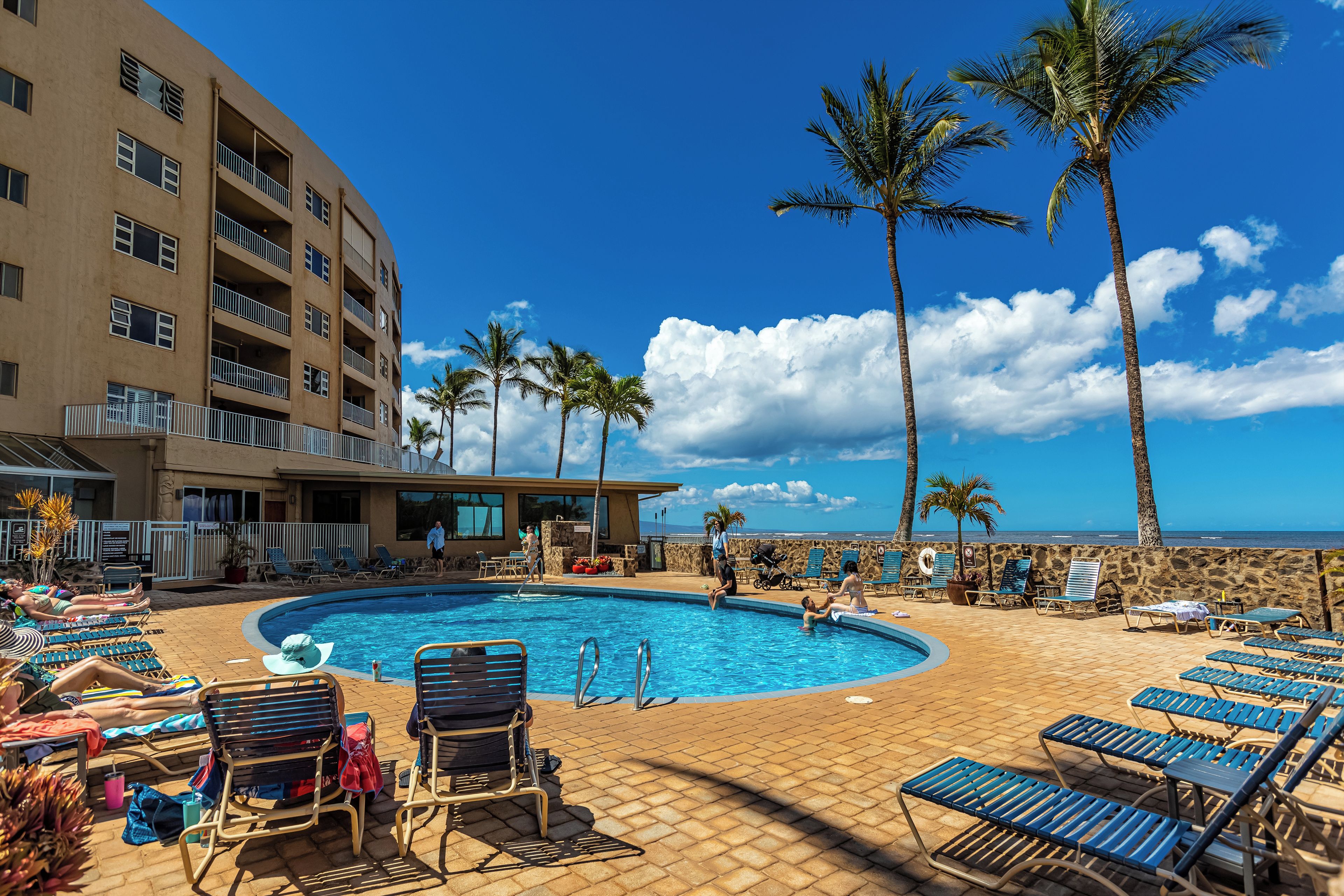 A pool area with lounge chairs, palm trees, and a building with balconies.