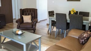 Un salon avec un canapé en cuir marron, une table basse en verre et un coin repas comprenant une table blanche et des chaises grises.