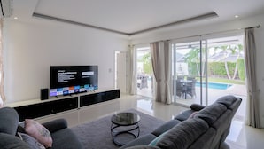 A modern living room with a flat-screen TV, comfortable seating, and a glass door leading to a pool area.