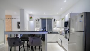 A modern kitchen with a central island, bar stools, a refrigerator, and a microwave.