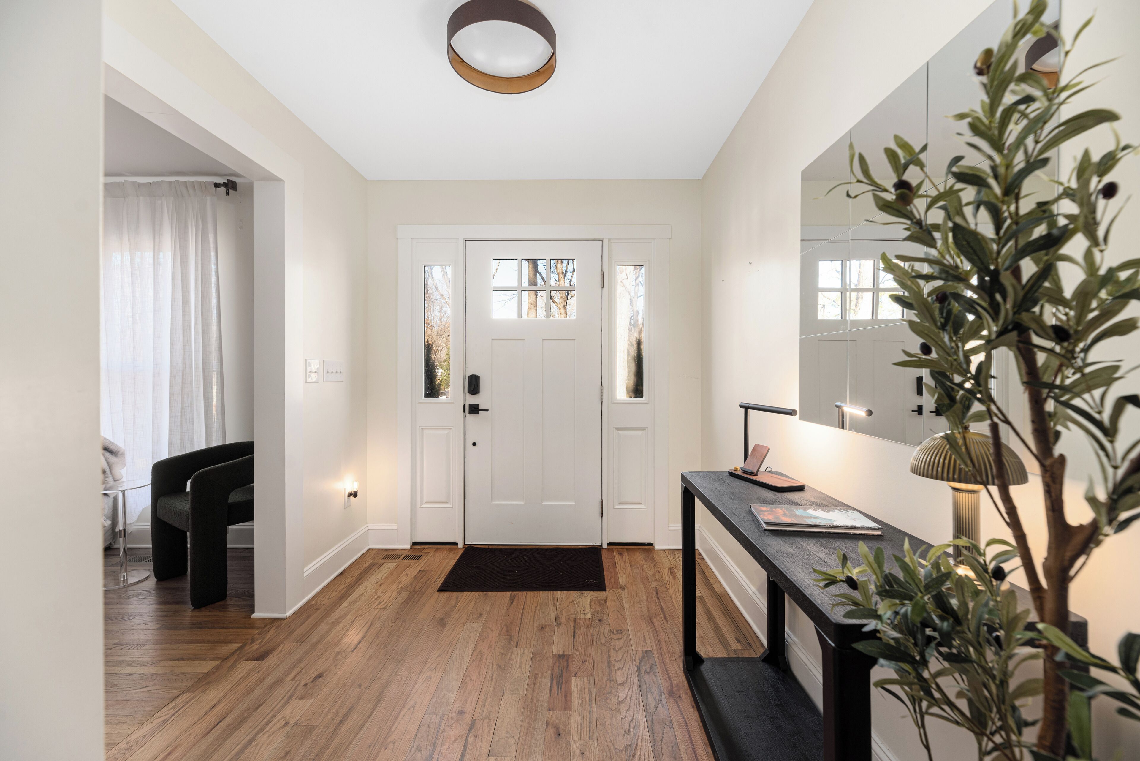 Un couloir avec un plancher en bois, un banc noir, une porte blanche et un miroir accroché au mur.