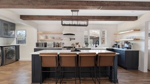 Een moderne keuken met een centraal eiland, barkrukken, houten balken en inbouwapparatuur.