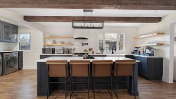 A modern kitchen with a central island, bar stools, wooden beams, and built-in appliances.