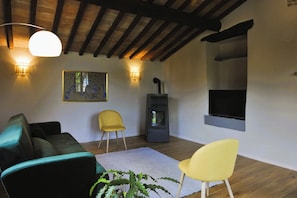 Un salon avec un canapé, deux fauteuils, une cheminée, un téléviseur et un tableau accroché au mur.