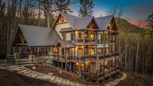 A multi-story log cabin with a wrap-around deck and multiple balconies, surrounded by a forested landscape. - Private Indoor Pool • Luxury Lodge • Theater, Firepit (Sevierville)