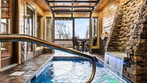 A hot tub area with a wooden deck, stone walls, and a view of the outdoors. - Private Indoor Pool • Luxury Lodge • Theater, Firepit (Sevierville)