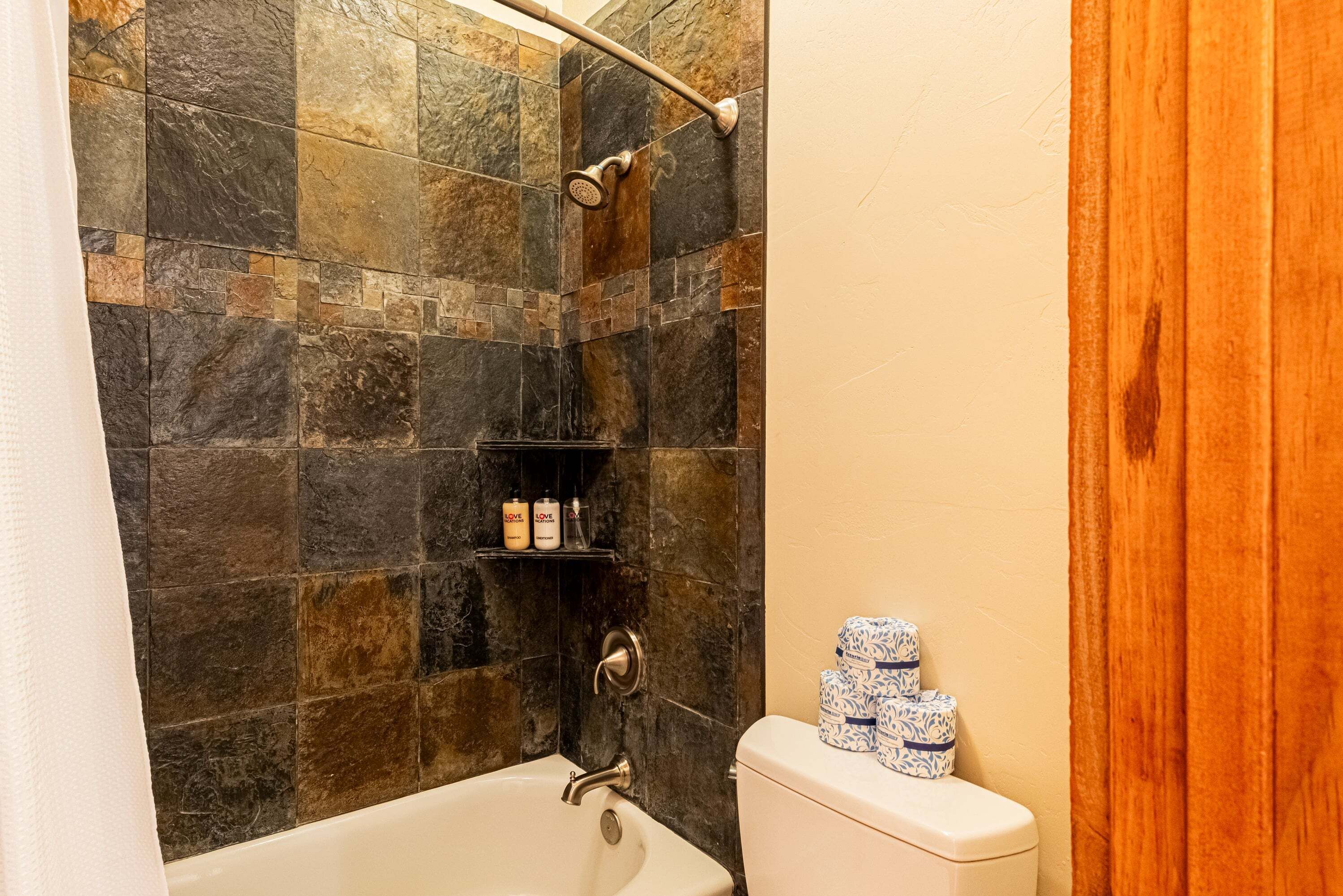 A bathroom with a bathtub, shower, and toilet. There are toiletries on a shelf.
