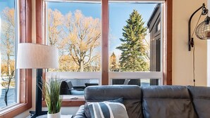 Una sala de estar moderna con un sofá de cuero, una mesa con una lámpara y vistas a árboles a través de amplios ventanales.