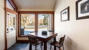 Un comedor con una mesa y sillas de madera, una puerta con paneles de vidrio y cuadros en la pared.