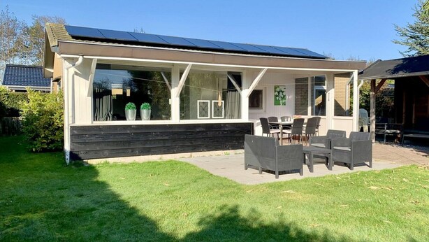 A modern house with a covered patio, solar panels, and a well-maintained lawn. - Great Bungalow Near the Beach and sea (Sint Maartensvlotbrug)