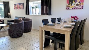A dining area with a wooden table, black chairs, and a window with curtains. There are two potted plants on the windowsill. - Great Bungalow Near the Beach and sea (Sint Maartensvlotbrug)