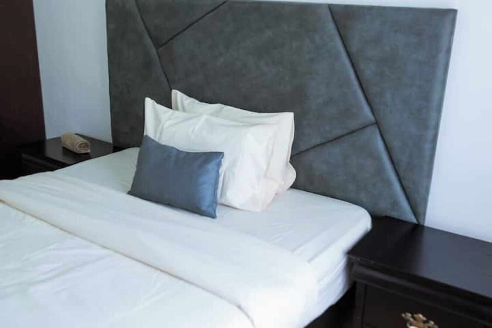 A neatly made bed with white bedding and two pillows, one grey and one white, in a room with a dark headboard.