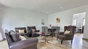 Un salón amplio con un sofá, dos sillones, una mesa de centro y una mesa de comedor con sillas.