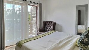 Un dormitorio con cama, una silla, un balcón con cortinas y un espejo.
