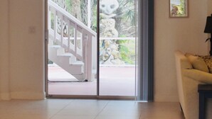 Ein geräumiges Zimmer mit einem großen Schiebeglasfenster, das zu einem Außenbereich mit Treppe und Grünpflanzen führt.