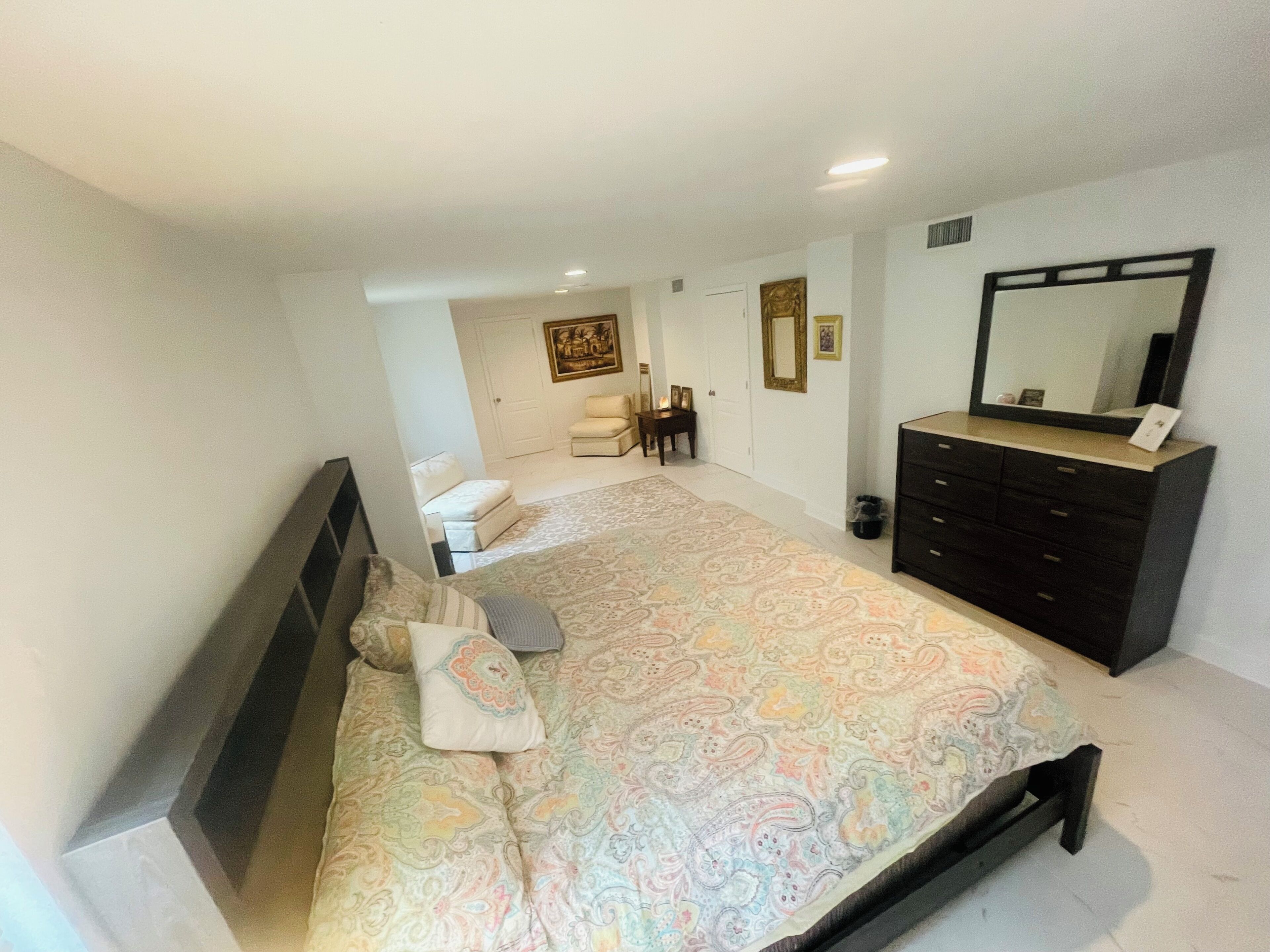 A bedroom with a large bed, a dresser, a chair, and a mirror.