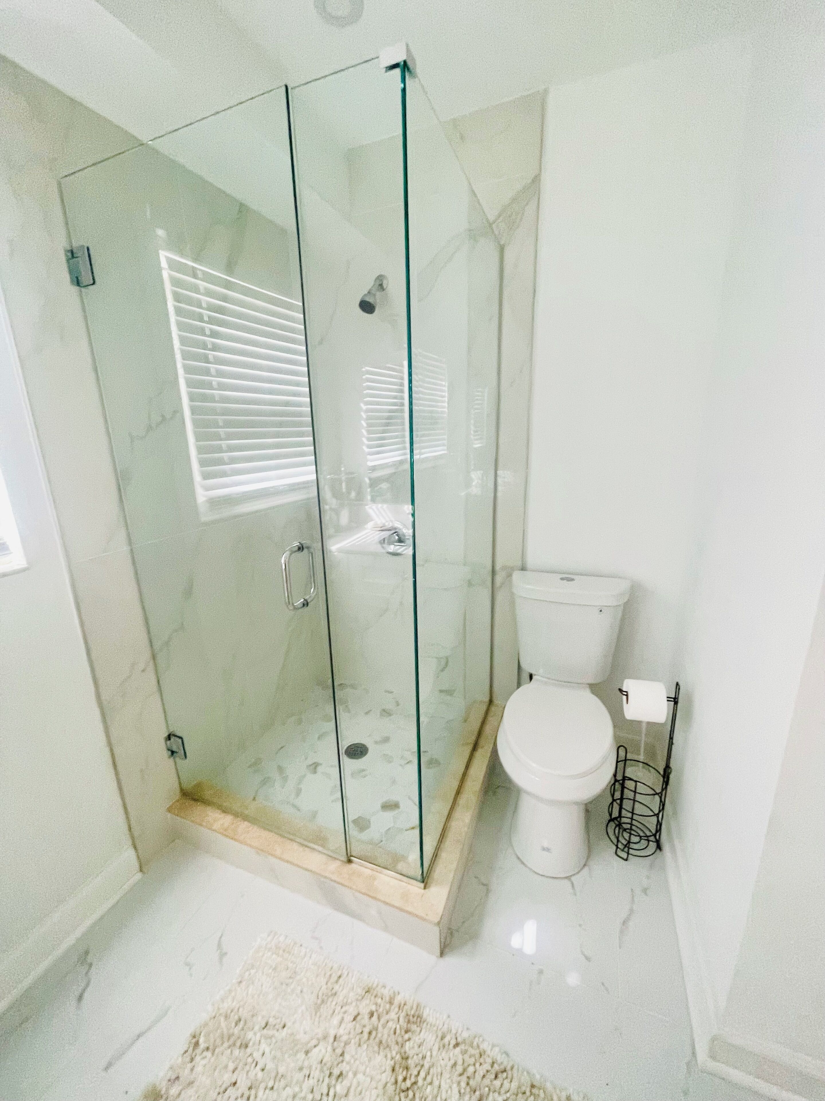 A modern bathroom with a glass-enclosed shower, a toilet, and a marble floor.