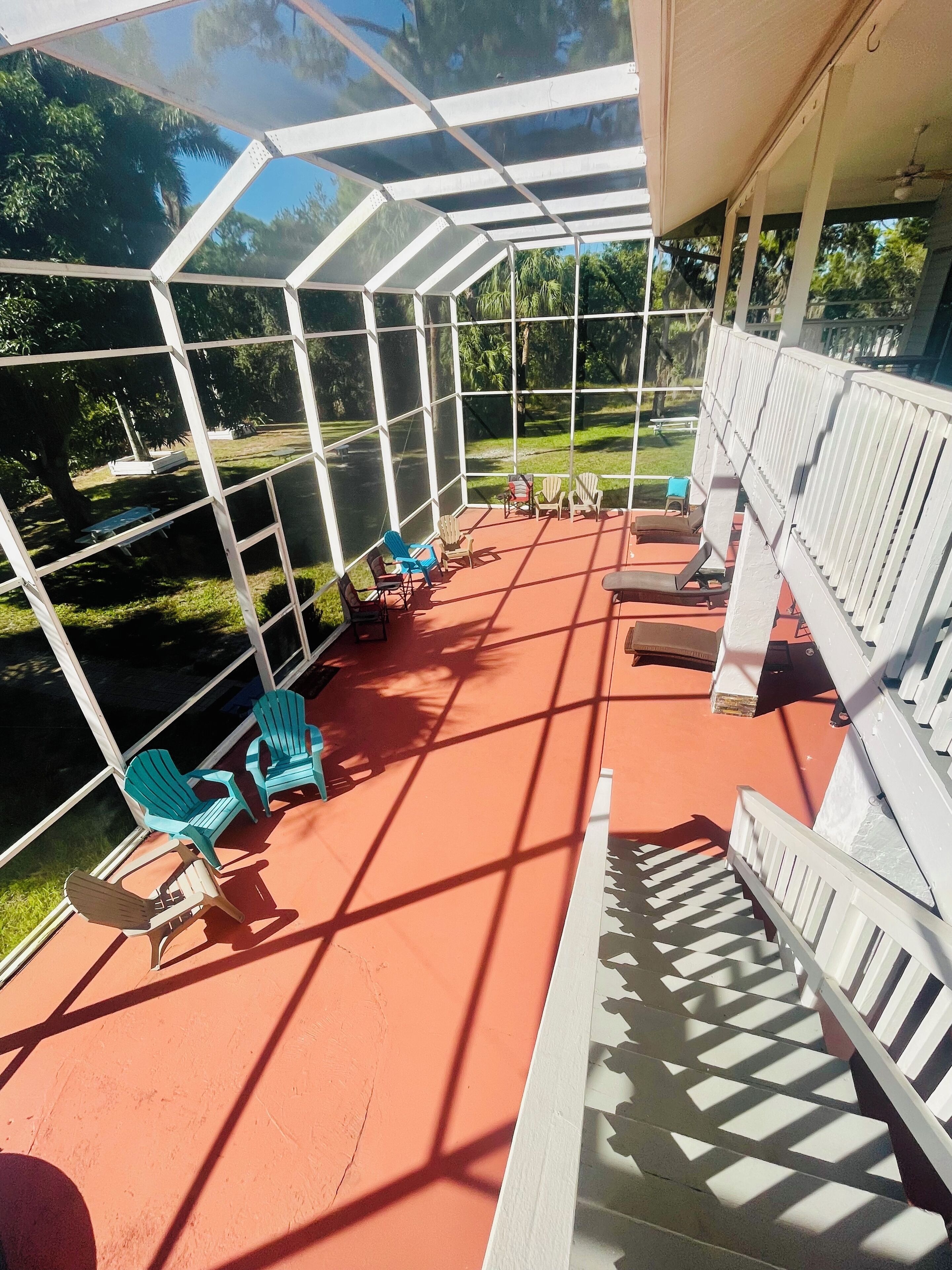 Un espace extérieur abrité, doté de chaises et de tables, entouré d’une clôture en métal blanc et donnant sur une pelouse.