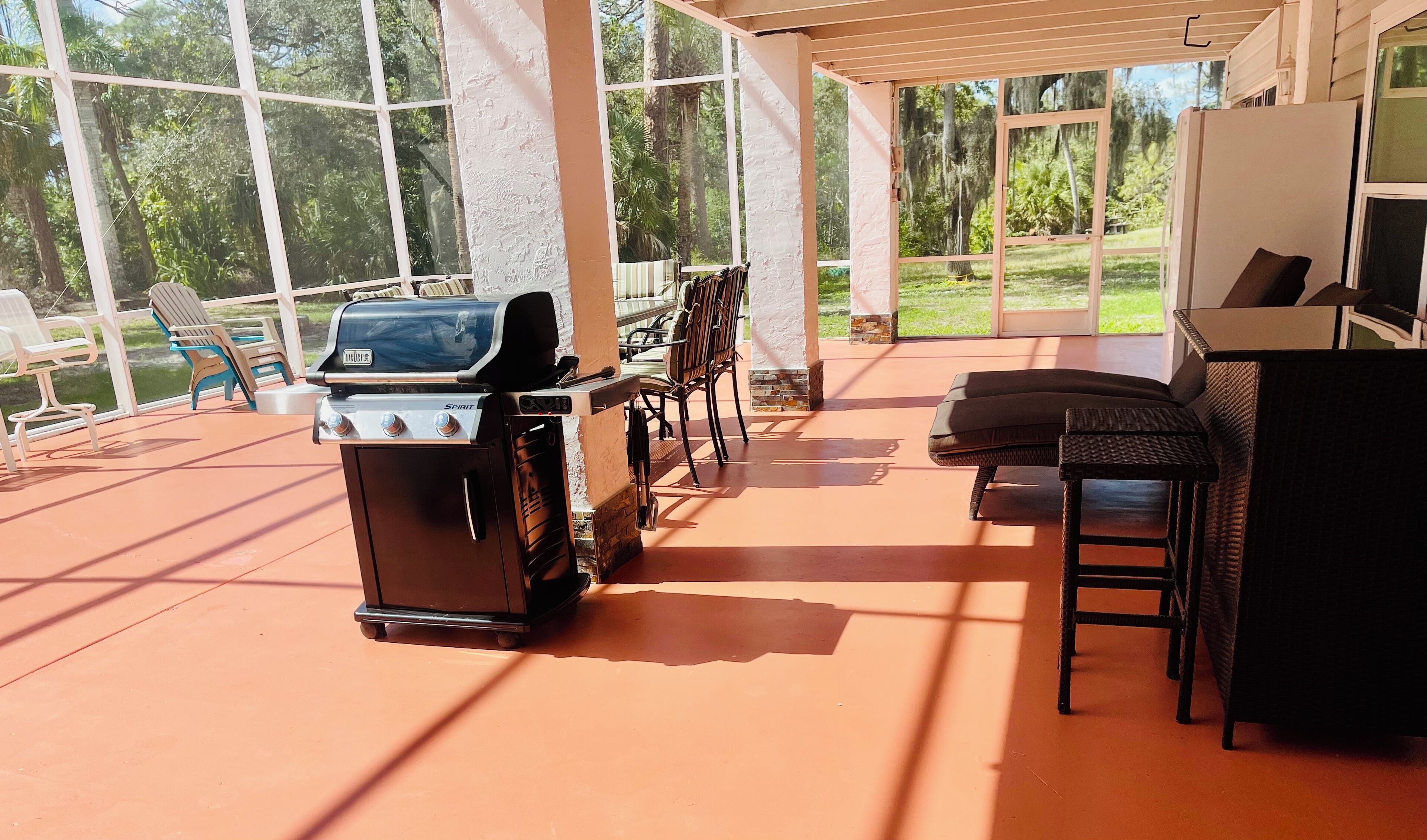 An outdoor patio with a Weber Spirit grill, wicker furniture, and a view of the surrounding greenery.