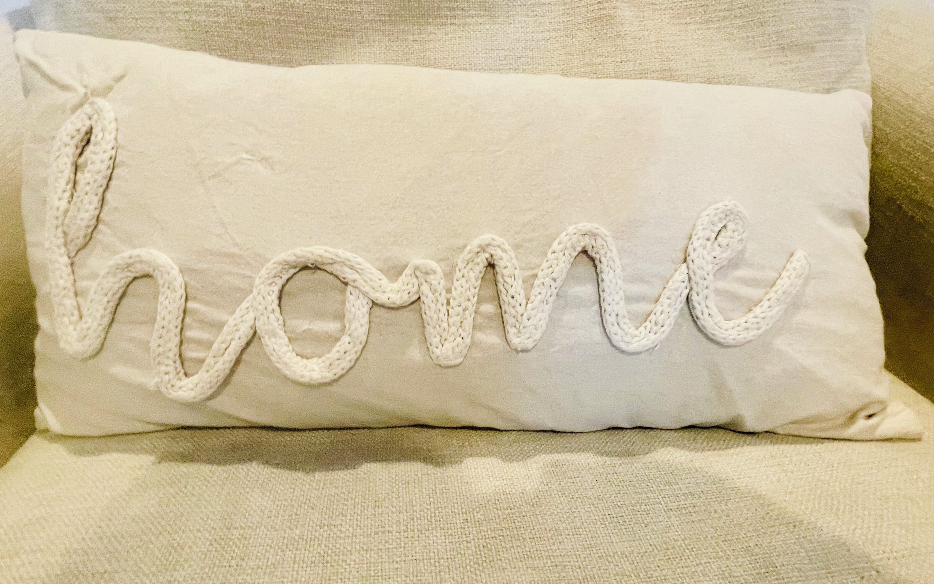 A beige pillow with the word "home" embroidered in a textured pattern.