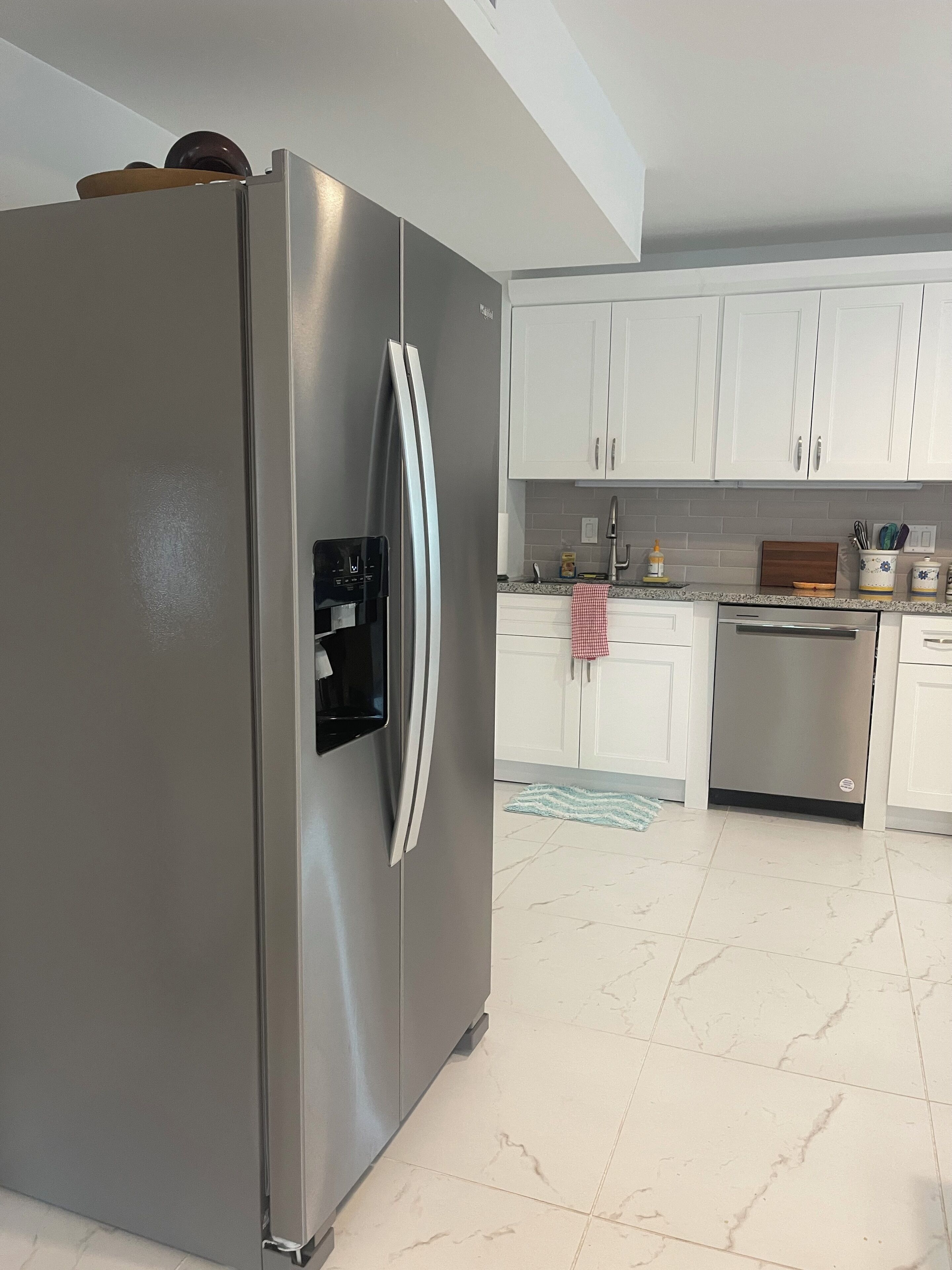 A modern kitchen with white cabinets, a stainless steel refrigerator, and a built-in dishwasher.