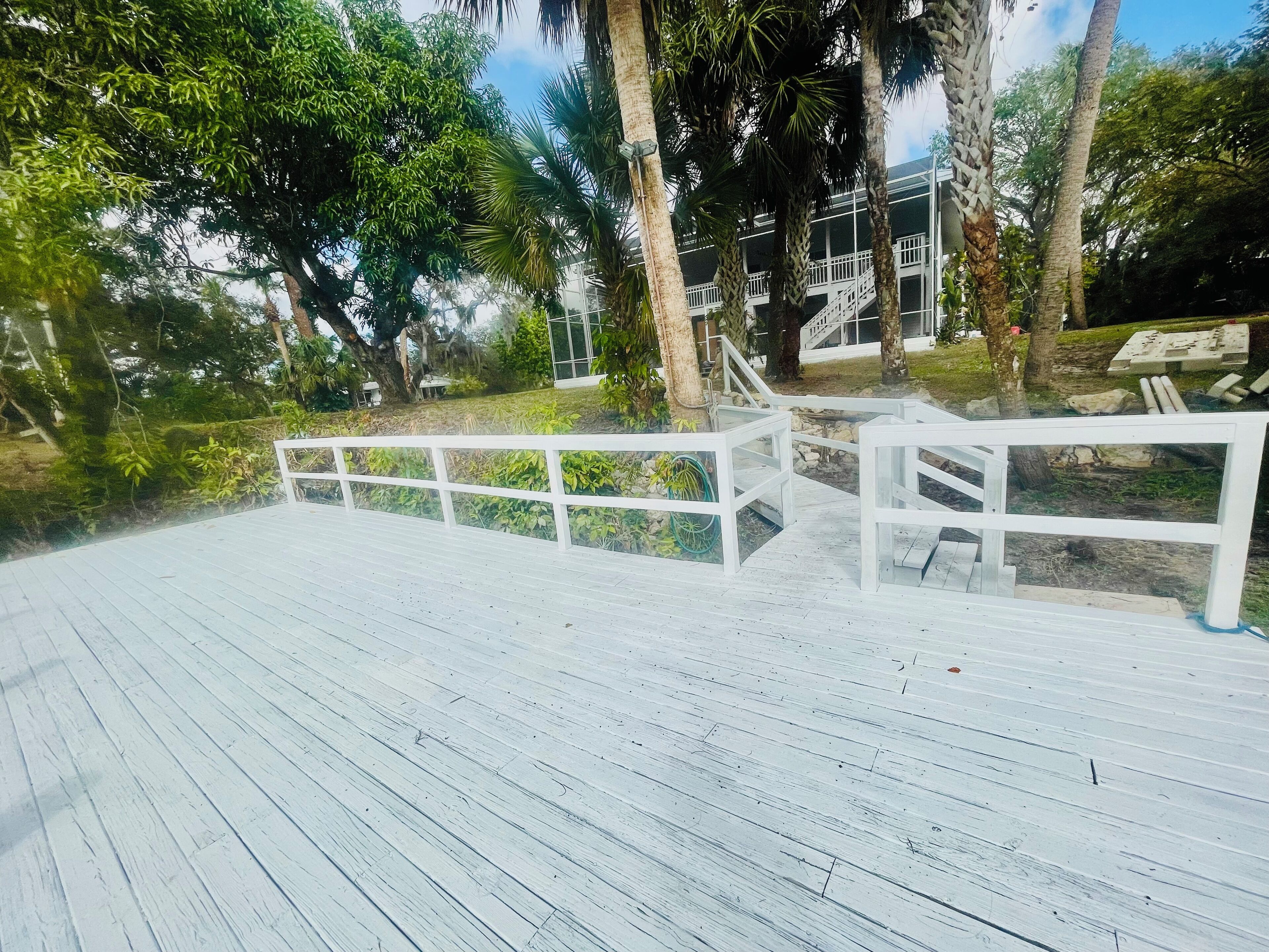 A wooden deck with white railings, surrounded by lush greenery and palm trees.
