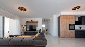 En moderne stue med en stor grå sofa, et fladskærms-tv og træskabe i det tilstødende køkkenområde.