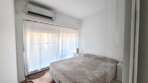A small, clean room with a bed, a bedside table, a heater, and a window with curtains. - Luminoso, muy Completo y Bien Ubicado (Buenos Aires)