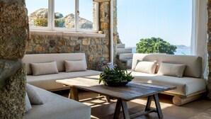 A cozy seating area with stone walls, a wooden table, and a view of the sea. - Villa Tavani Agios Ioannis Mykonos (Mykonos)