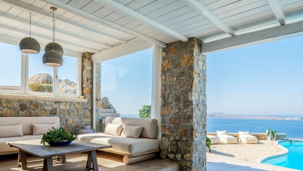 A sunlit interior with stone walls, a sofa, a table, and a view of the sea. - Villa Tavani Agios Ioannis Mykonos (Mykonos)