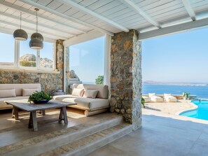 A sunlit interior with stone walls, a sofa, a table, and a view of the sea. - Villa Tavani Agios Ioannis Mykonos (Mykonos)