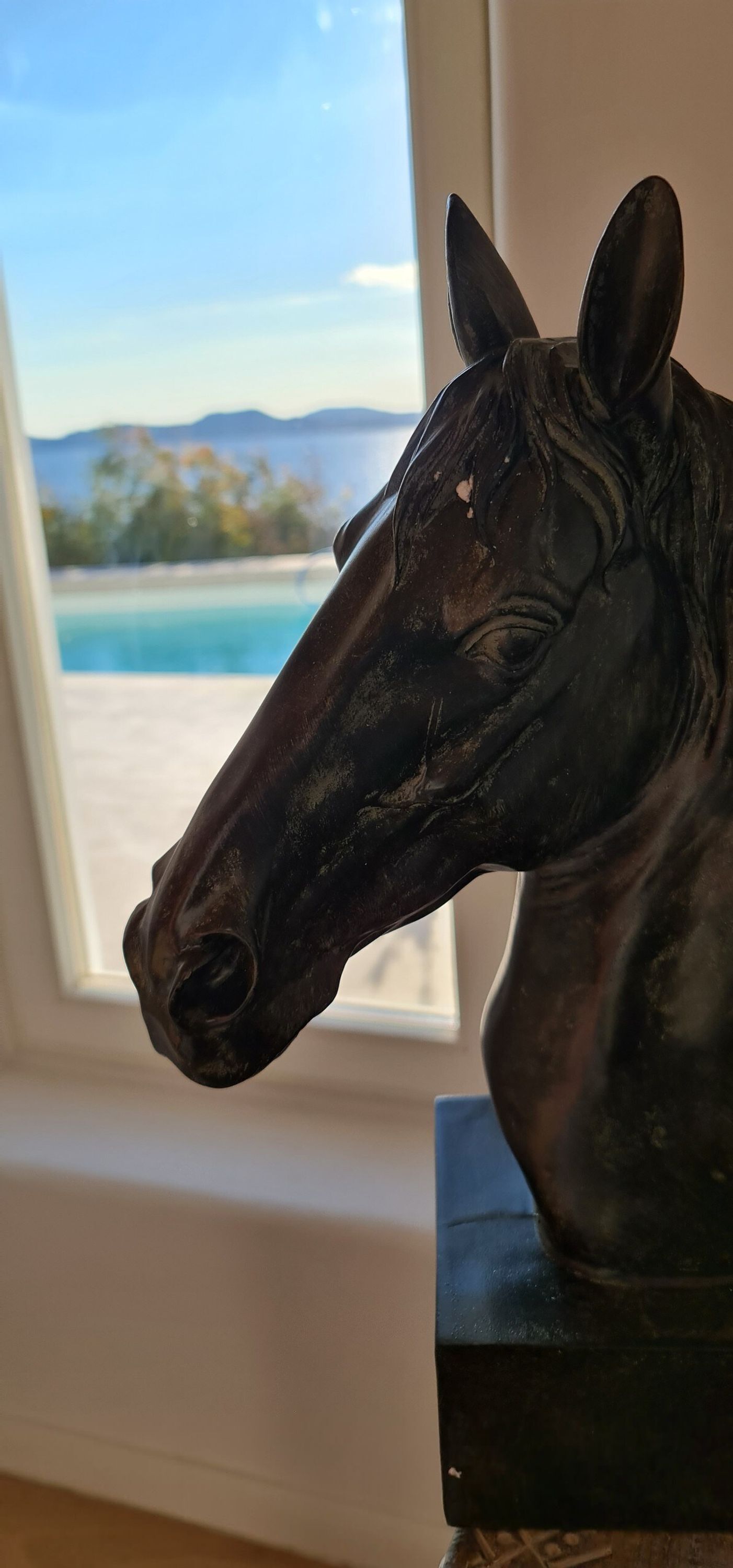 En häststaty i ett rum med ett fönster som vetter ut mot en pool och berg.
