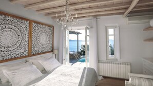 Een slaapkamer met een groot bed, een kroonluchter, uitzicht op zee en een houten plafond.