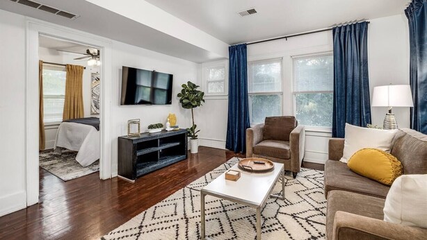 A living room with a flat-screen TV, a sofa, a chair, a coffee table, and a plant. - Pet-friendly Furnished Apt Near Emu Free Parking 2 Bedroom Apts (Ypsilanti)