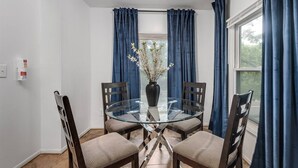 A dining area with a glass table surrounded by four chairs, a vase with flowers, and blue curtains. - Pet-friendly Furnished Apt Near Emu Free Parking 2 Bedroom Apts (Ypsilanti)
