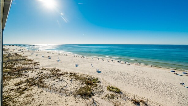 A beach with a clear sky, a pier in the distance, and a fence along the shoreline. - Island Sunrise 663 2 Bedroom Condo (Gulf Shores)