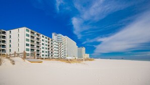 A beachfront hotel with multiple floors, balconies, and a sandy beach in the foreground. - Island Sunrise 663 2 Bedroom Condo (Gulf Shores)