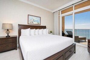 A hotel room with a large bed, a nightstand with a lamp, a painting on the wall, and a balcony with a view of the sea. - Phoenix Gulf Towers 1007 3 Bedroom Condo (Orange Beach)