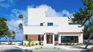 A modern two-story building with a white facade, large windows, and a small entrance. - Halcyon Point: New Luxurious Oceanfront Villa w/ Pool, Spa + Tanning Terrace (Grand Cayman)