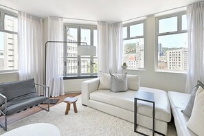 A modern living room with a white sofa, grey sofa, and a grey sofa bed. There is a floor lamp, a small wooden stool, and a white coffee table. - Elevated Luxury 2-Bed Apt with Elevator Access (Cape Town)