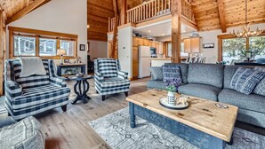 Ein gemütliches Wohnzimmer mit hohen Decken, karierten Sofas, einem Holztisch und Blick zur Küche und oberen Etage.